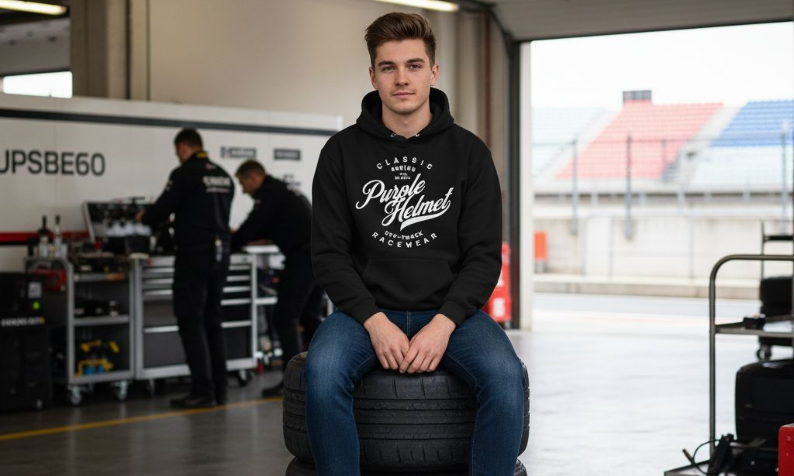Person sitting on a tire in a garage wearing a hoodie with branding.